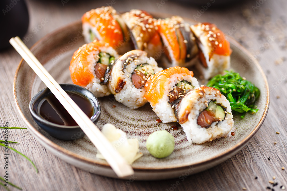 Sushi maki rolls with salmon, eel, avocado, cucumber on a plate with chopsticks, soy sauce, wasabi and ginger. Japanese traditional fish food closeup served for lunch in modern gourmet restaurant Sushi maki rolls with salmon, eel, avocado, cucumber on a plate with chopsticks, soy sauce, wasabi and ginger. Japanese traditional fish food closeup served for lunch in modern gourmet restaurant