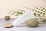 White empty tube for cream on the stone. Mockup tube on beige background with green leaf