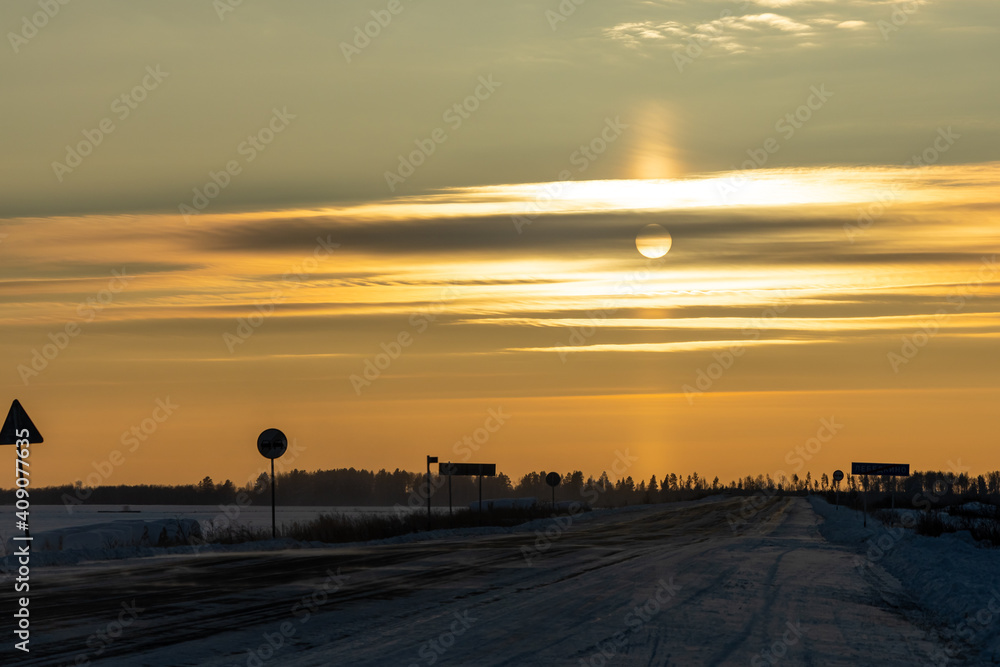 Snowy deserted road in winter on the orange sunset background