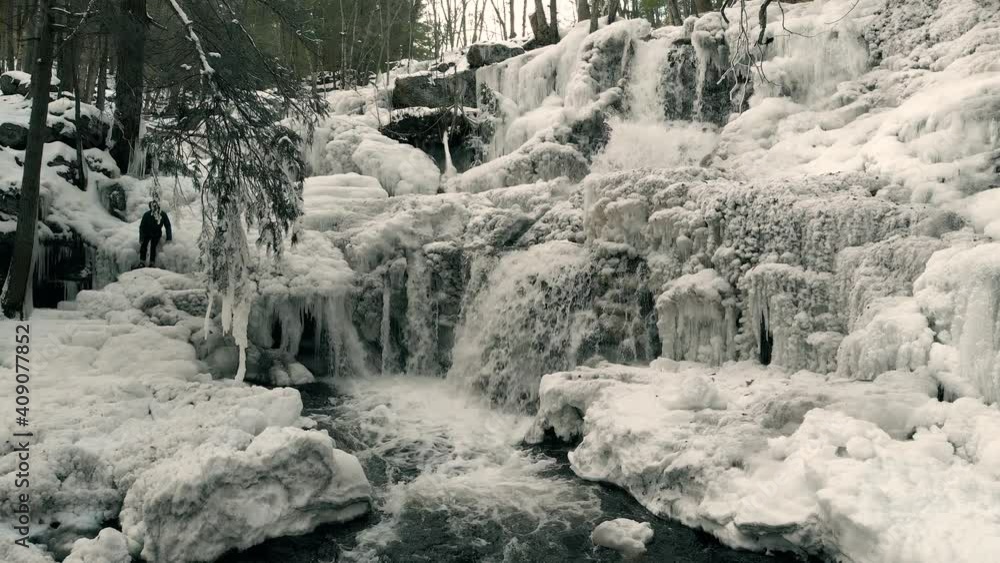 Aerial shot of frozen waterfall with running water. Person climbing down ice shelves. Aerial shot of frozen waterfall with running water. Person climbing down ice shelves.