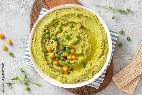 Spicy hummus of green peas and chickpeas in a white bowl on a grey background top view. Healthy appetizer, vegan food, vegetarian snack. 