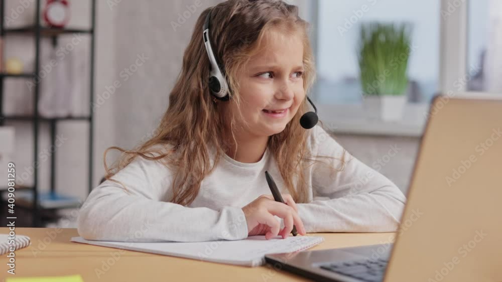 Schoolgirl in headset has online lesson, video call zoom with teacher, answering questions,check of knowledge.Cute primary school girl studying at home using laptop. Distance learning. Home education Schoolgirl in headset has online lesson, video call zoom with teacher, answering questions,check of knowledge.Cute primary school girl studying at home using laptop. Distance learning. Home education