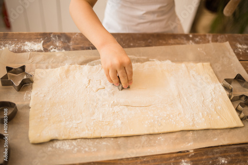 a child's hand cuts the dough with gingerbread molds on a wooden table