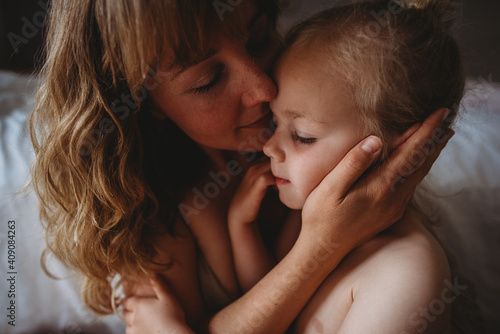 Gorgeous mother and daughter with closed eyes kissing at home photo