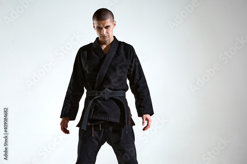 Sportive frowning man in black kimono for karate or kudo on white studio background with copy space © Georgii