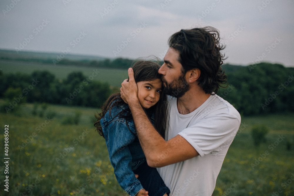 Father carrying and kissing daughter outdoors in field Father carrying and kissing daughter outdoors in field