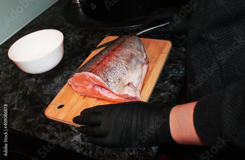 Female hands in gloves cut red fish in the kitchen.