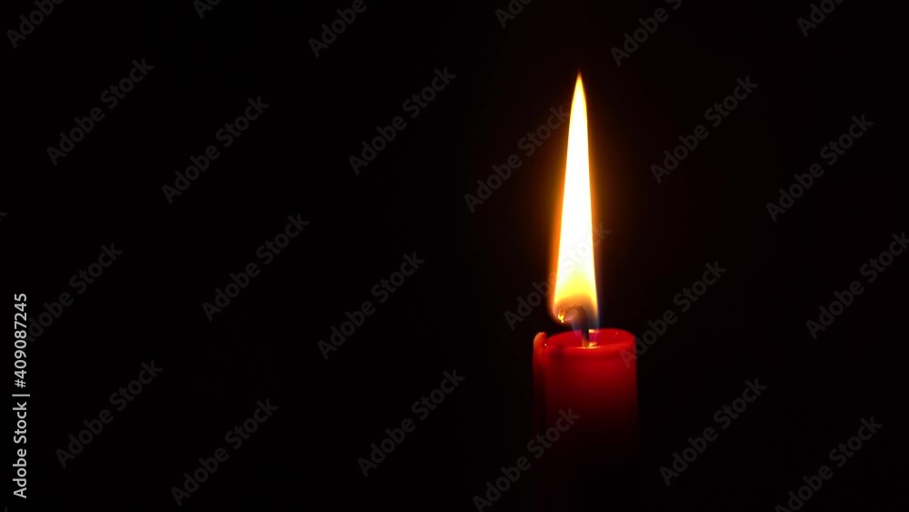 Red candle burns and flickers in blackness: space to the left for text. Red candle burns and flickers in blackness: space to the left for text.
