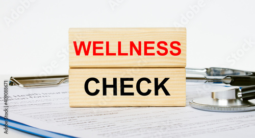 Wooden blocks with text Wellness Check on a clipboard and a stethoscope