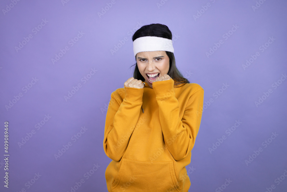 Young latin woman wearing sportswear over purple background very happy and excited making winner gesture with raised arms, smiling and screaming for success. Young latin woman wearing sportswear over purple background very happy and excited making winner gesture with raised arms, smiling and screaming for success.