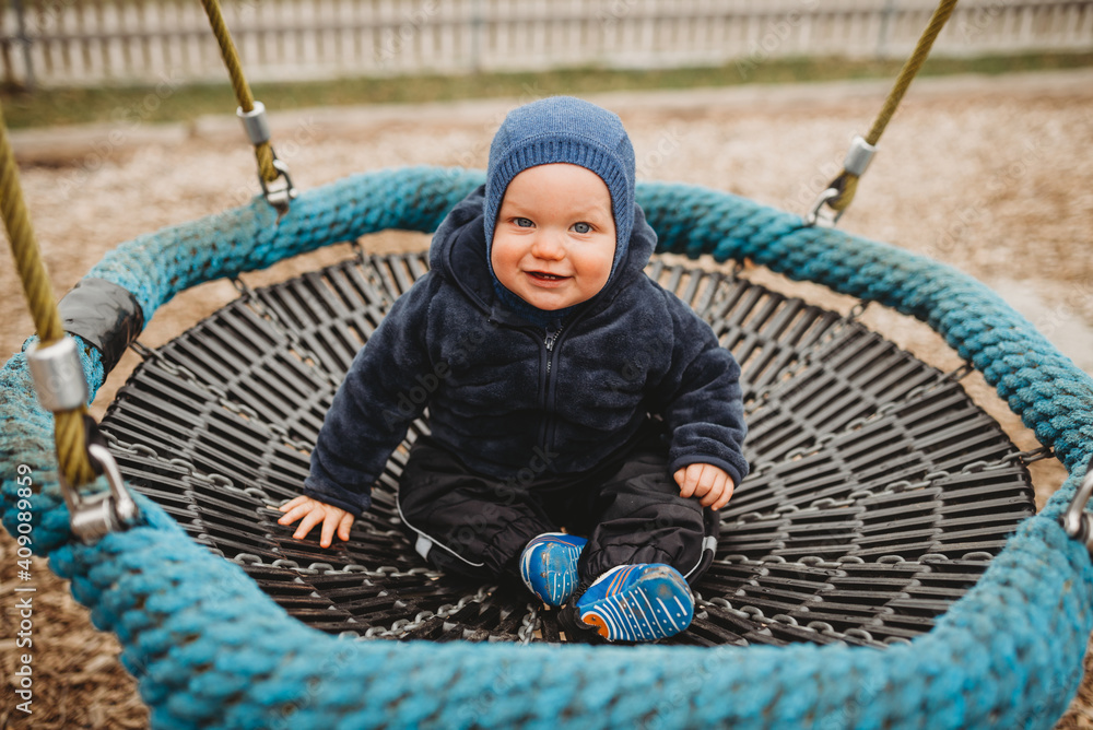Baby boy wearing blue in playground nest hammock smiling in winter Baby boy wearing blue in playground nest hammock smiling in winter
