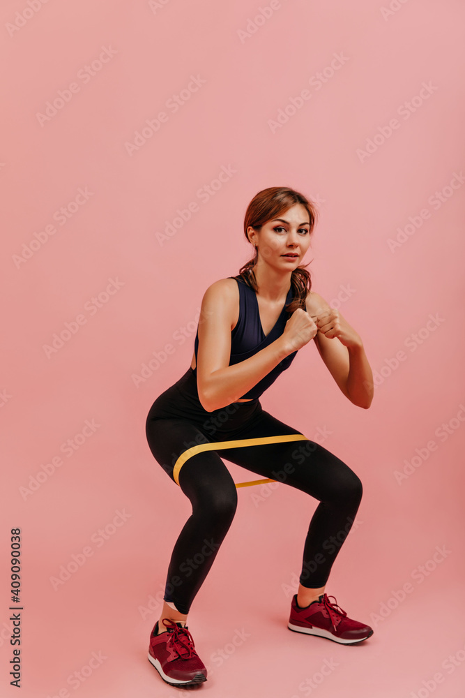 Strong fitness trainer does exercise to strengthen legs and buttocks. Snapshot of girl squatting on isolated background
