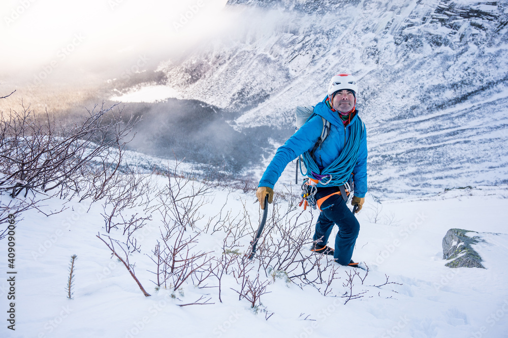 male alpine climber ascends steep section of snow with mountains male alpine climber ascends steep section of snow with mountains