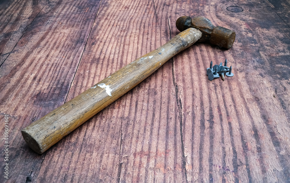 Vintage wooden handled hammer and heap of small nails on a rustic wooden bench