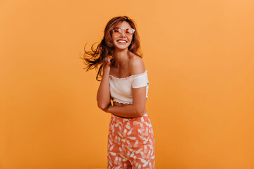 Tanned American girl with stylish haircut poses, looking at camera with smile. Portrait of joyful lady in summer outfit