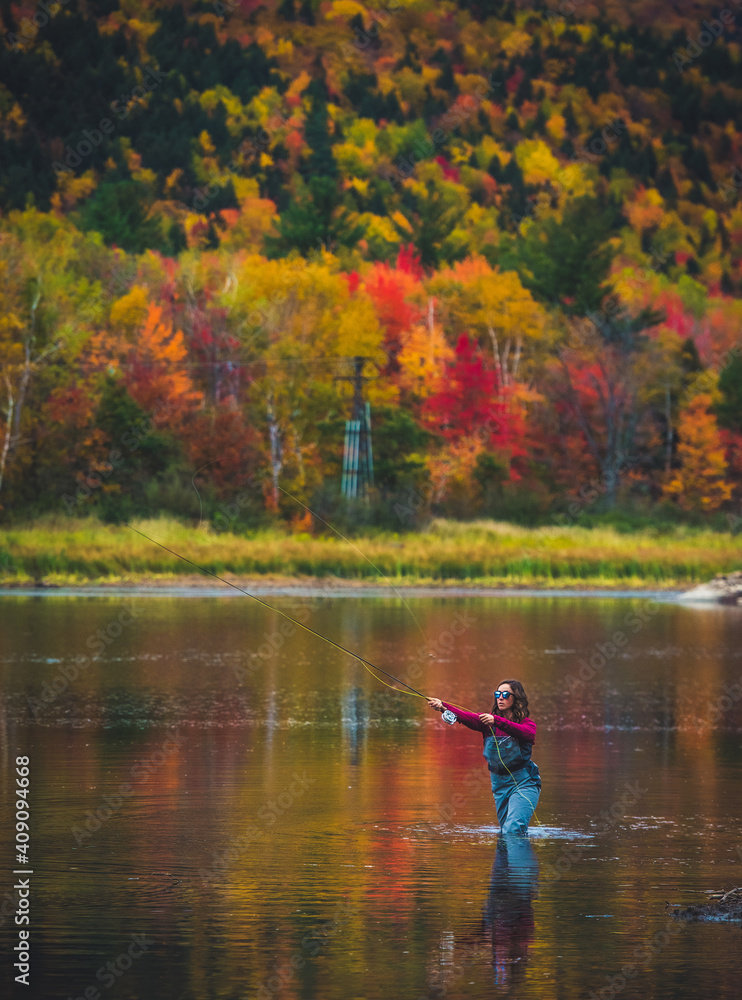 Female angler casting into river with bright foliage Female angler casting into river with bright foliage