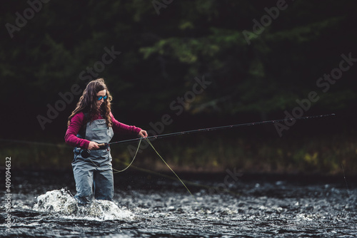 Woman angler in waders walks through rushing water in river photo