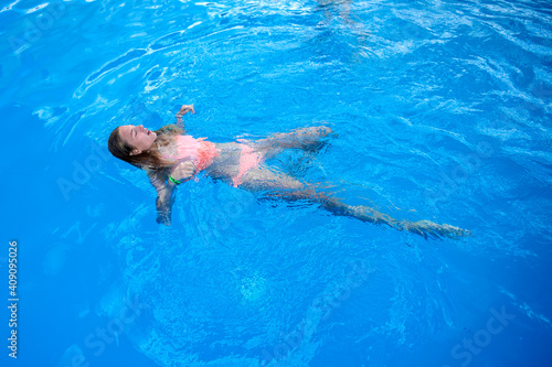 Teenager girl swims in the pool. Happy teenage girl swimming in blue transparent water in swimming pool at aquapark