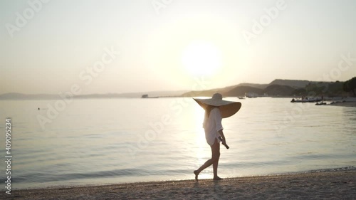 Middle shot of girl in a big hat walking near the sea of Greece. Young woman wearing a big hat and sunglasses is walking on the coastline of Khalkidhiki island and watching the sunset. High quality photo