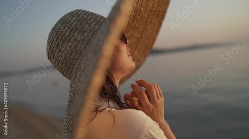 Close-up portrait of a girl wearing a big hat and watching the sunset on Khalkidhiki island. Young lady in a big hat is seating near the sea of Greece and watching the sunset. High quality FullHD photo