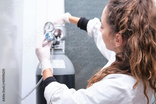 Young female scientist opening a gas cylinder with pressure gauge in a specialized laboratory. Laboratory research concept.