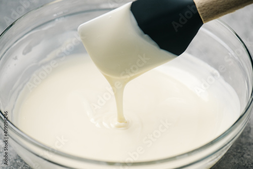 Melted white chocolate dripping from a spatula into a mixing bowl