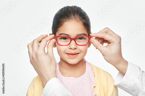 Ophthalmologist tries on eyeglasses of a Latin American little girl, close-up. Treatment of children's vision with glasses