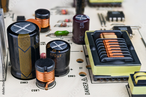 Electronic components on printed circuit board detail. Close-up of capacitors, inductors and rectangular transformer with protruding insulation grooves in copper wire winding. Electrical engineering.