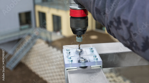 Closeup of drilling holes using a jig bushing for precise guide of twist drill bit. Boring template of acrylic and aluminum. Assembly stainless steel handrail to terrace railing in apartment building. photo