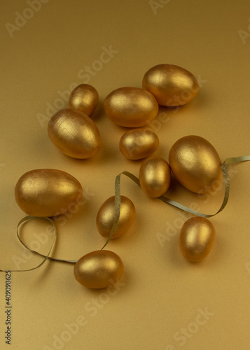 Decorative wooden Easter eggs painted gold on yellow-gold background. Happy Easter greeting card.