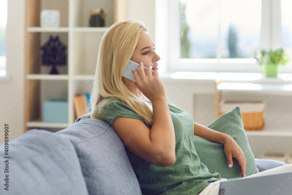 Freelance, distant working, online communication concept. Profile of positive blonde woman sitting on sofa at home and talking on phone with colleague keeping social distance during quarantine Freelance, distant working, online communication concept. Profile of positive blonde woman sitting on sofa at home and talking on phone with colleague keeping social distance during quarantine