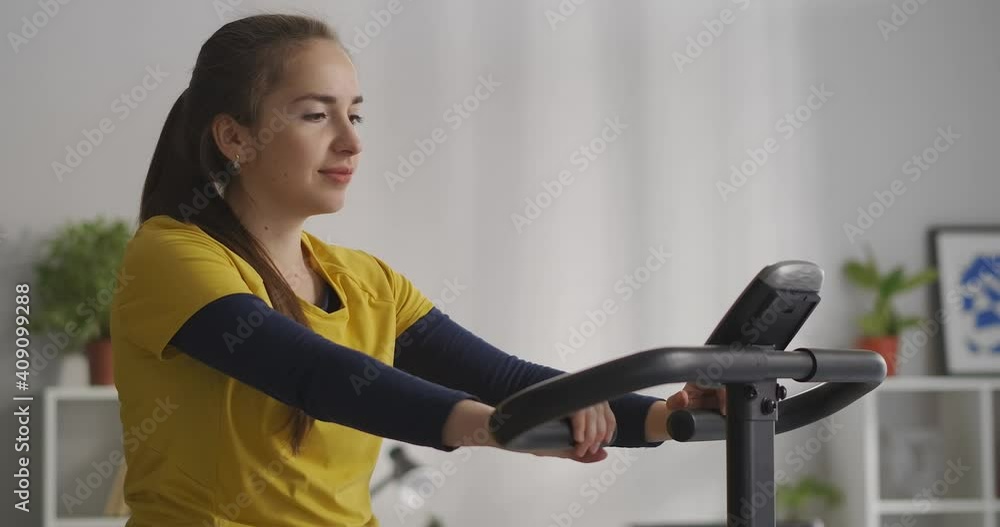 calm young woman is exercising with stationary bicycle at home, sport activity and healthy lifestyle, medium portrait calm young woman is exercising with stationary bicycle at home, sport activity and healthy lifestyle, medium portrait