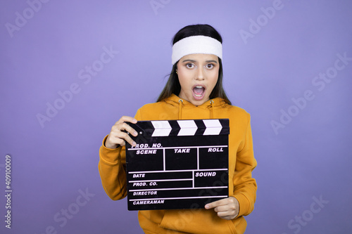 Young latin woman wearing sportswear over purple background holding a clapperboard © Irene