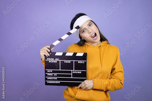 Young latin woman wearing sportswear over purple background holding a clapperboard © Irene
