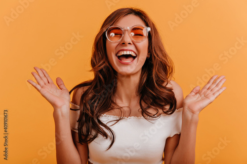 Photo taken in studio of emotional, positive girl, genuinely laughing at good joke. Wavy haired teen wants to clap her hands