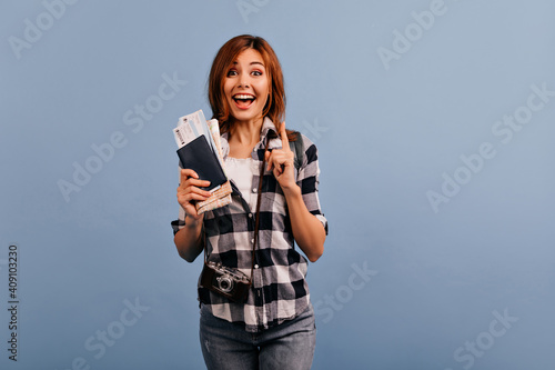 Cute girl came up with how to have fun and bought plane ticket. Indoor portrait of lady in white T-shirt and jeans, who had cool idea