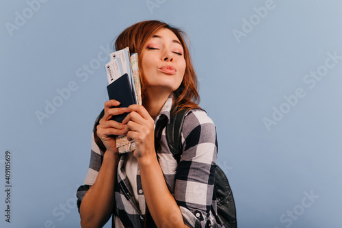 European model with nude make-up is blowing kiss, holding important tickets and card near his face. Closeup portrait of charming traveler