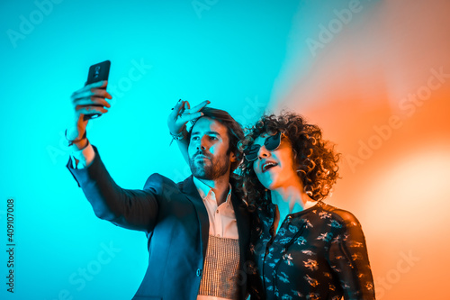 Party lifestyle, a Caucasian couple taking a selfie at a party with orange and blue lights © unai