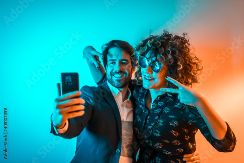 Party lifestyle, a Caucasian couple in love taking a selfie at a party with orange and blue lights, on Valentine's Day