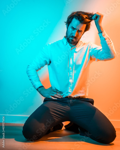 Studio lifestyle, sweet look of a Caucasian man in a white shirt, illuminated with an orange and blue neon light