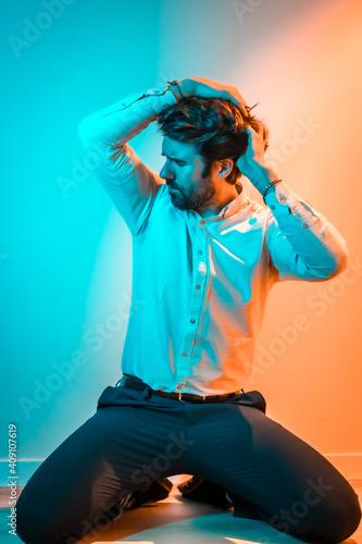 Studio lifestyle, sweet look of a Caucasian man in a white shirt, illuminated with an orange and blue neon light