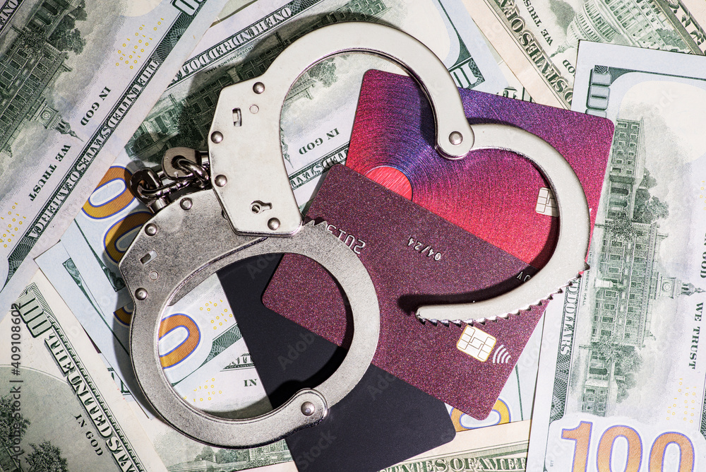 Steel handcuffs and credit cards lying on the background of american dollars. Dollar and credit cards with handcuffs. Financial crimes