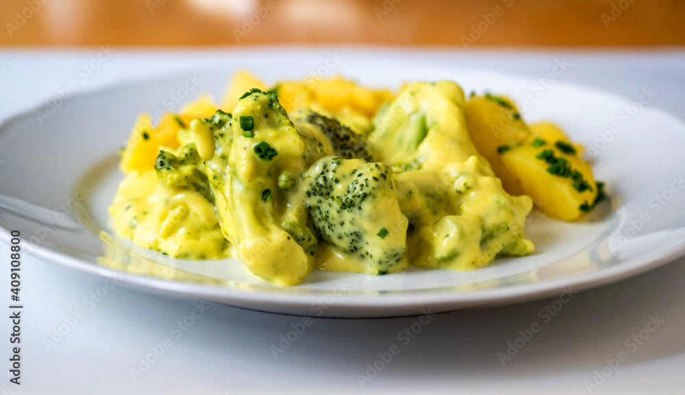 Stewed broccoli in creamy sauce with potato on white plate.