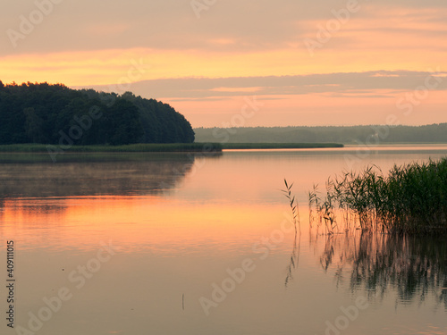 Sunrise reflection landscape. Orange sky and water. Seksty lake, Masuria in Poland.