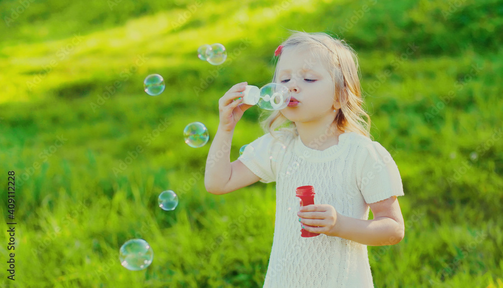 Portrait of little girl child blowing soap bubbles in summer park