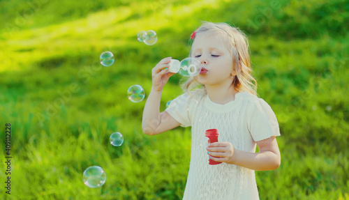 Portrait of little girl child blowing soap bubbles in summer park