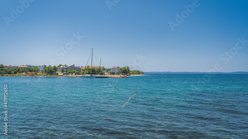 Yachts or sailboats moored at clear waters of Zaton bay with rocky coastline. Houses or resorts at the edge of turquoise water of Adriatic Sea Croatia