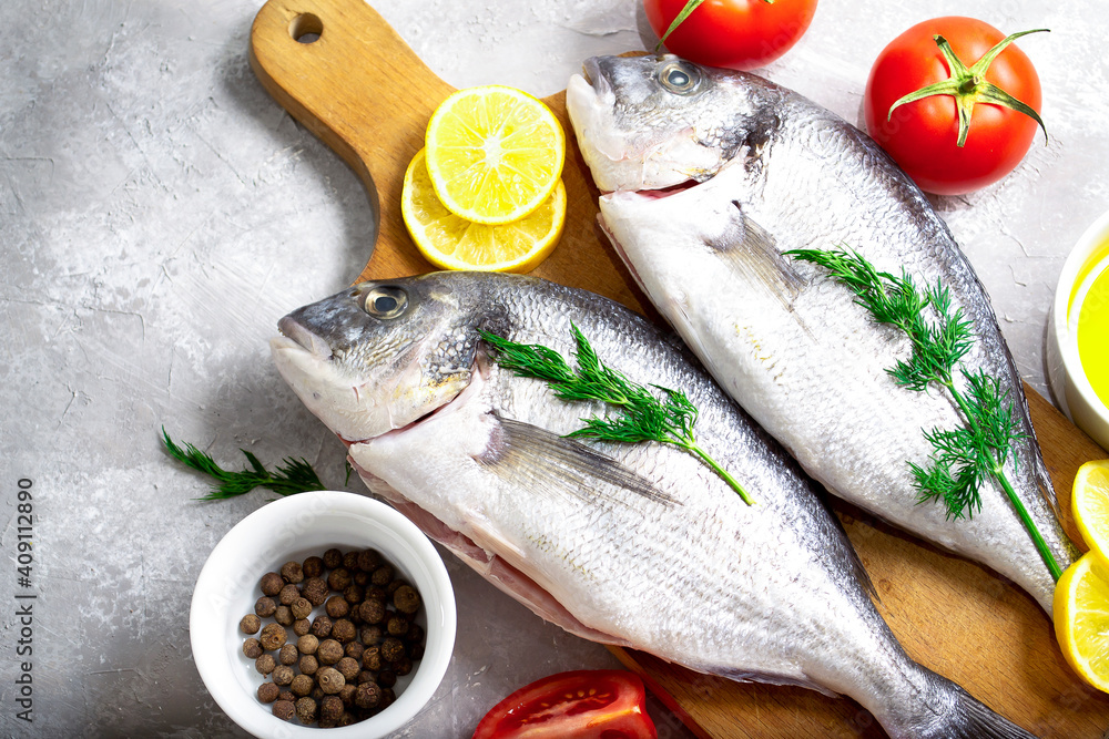 Dorado fish raw on a wooden board with cooking ingredients such as tomatoes, lemons, herbs, pepper and oil Dorado fish raw on a wooden board with cooking ingredients such as tomatoes, lemons, herbs, pepper and oil