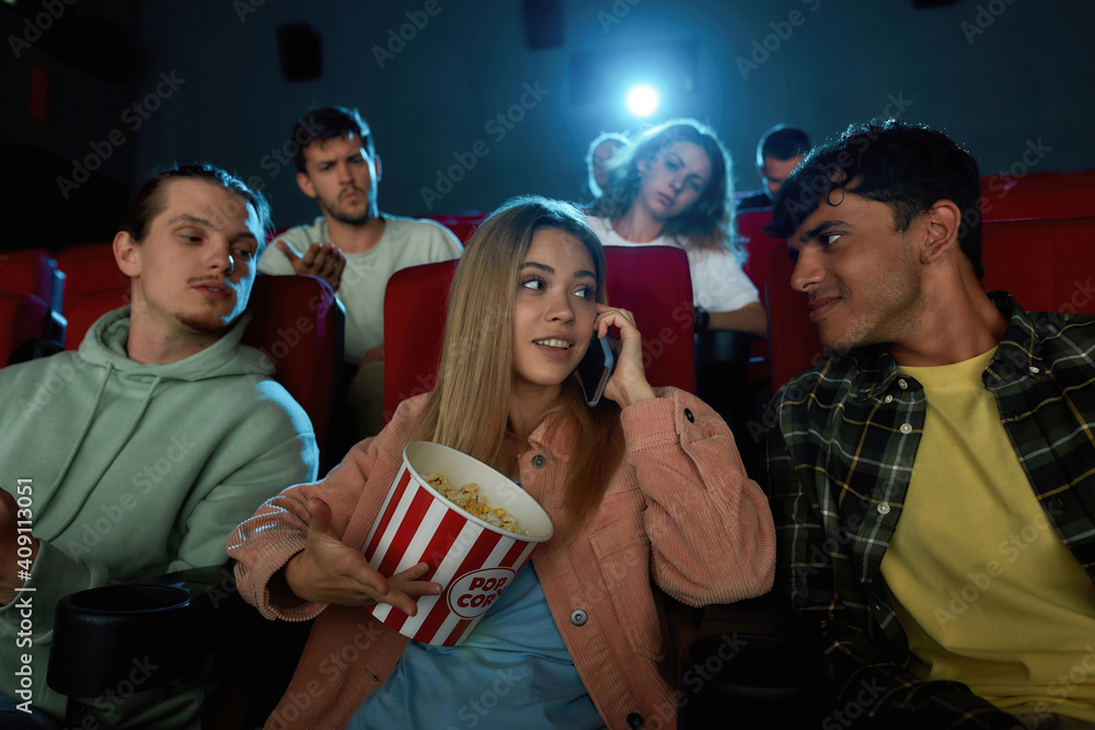 Cheerful young woman talking on the phone, annoying audience while watching movie with friends at the cinema