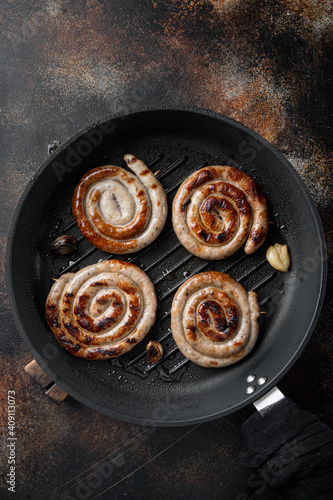 Grilled pork meat sausages in cast iron frying pan, on old dark rustic background, top view flat lay